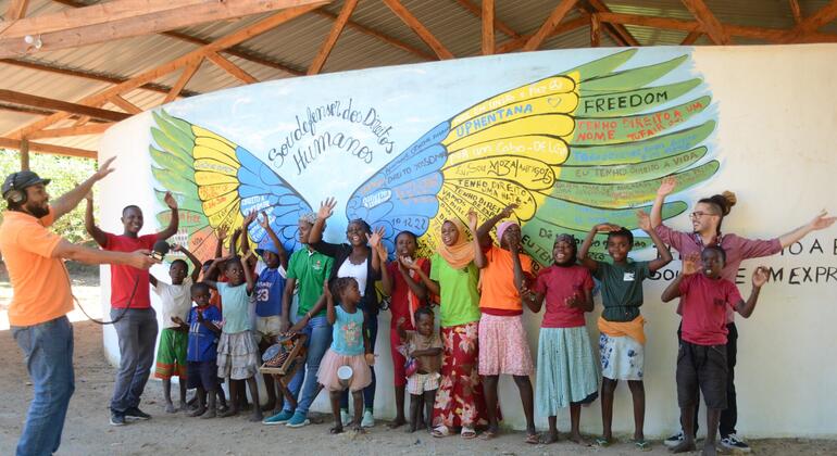 Um grupo de adultos e crianças posa diante de um mural colorido com as palavras "FREEDOM" e "Direitos Humanos" em Moçambique.