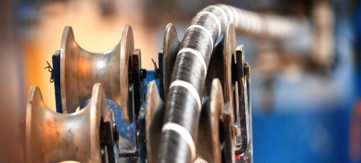 A close-up view of a submarine cable being wound onto a large industrial reel, highlighting the intricate details of the cable and machinery used in its deployment.