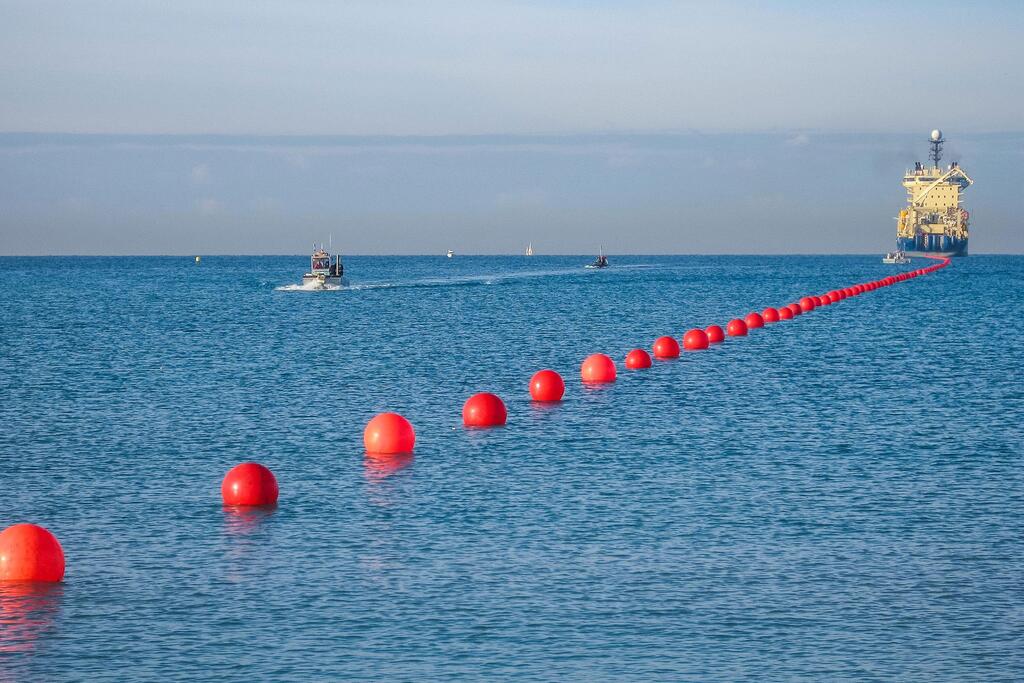 Une ligne de marqueurs de bouées rouges dans l'océan, avec un navire de pose de câbles et de petits bateaux à distance, représentant le Sommet international sur la résilience des câbles sous-marins de 2026.