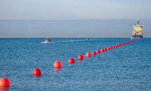 Una línea de marcadores de boyas rojas en el océano, con un buque de colocación de cables y pequeñas embarcaciones en la distancia, representando la Cumbre Internacional de Resiliencia de Cables Submarinos 2026.