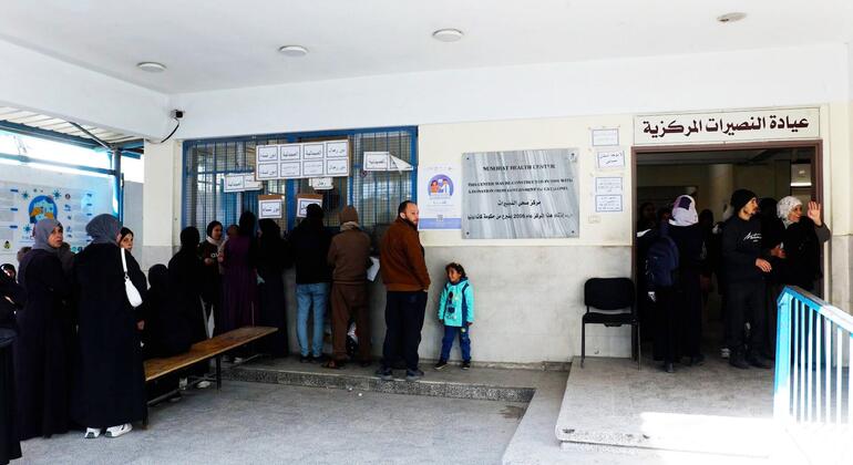 المرضى ينتظرون في صف في مركز نسيرات الصحي، وهو عيادة تديرها الأونروا في غزة، مع إشارة عربية مرئية على الحائط.