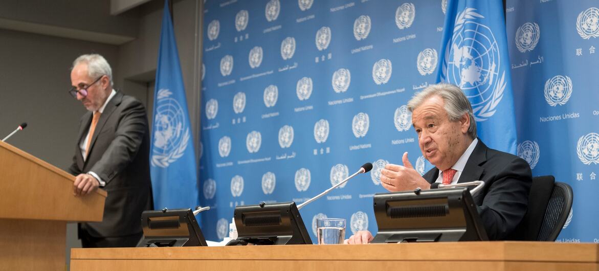Secretary-General António Guterres (seated at right) speaks to reporters at a press conference at the UN Headquarters, in New York. Standing nearby is his spokesperson, Stéphane Dujarric.