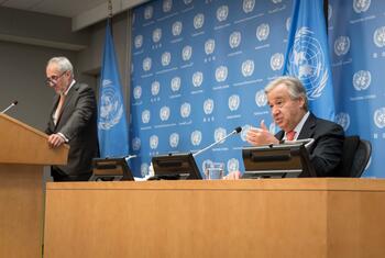 الأمين العام أنطونيو غوتيريش يتحدث في مؤتمر صحفي، يجلس على المنصة مع علمات الأمم المتحدة وعلامات في الخلفية. يقف بالقرب من المتحدث باسمه، ستيفان دوجاريك.