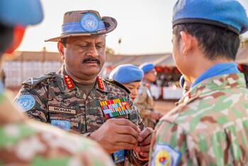 यूएनएमआईएसएस बल के कमांडर, जो मोहन के रूप में पहचाने जाते हैं, को दक्षिण सूडान में एक शांति सैनिक के साथ बातचीत करते हुए देखा जाता है, दोनों संयुक्त राष्ट्र वर्दी और नीले बैरेट पहने हुए हैं।