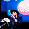 Maria Semushkina se presenta en el escenario del festival 'Music Saves the World', cantando con un micrófono mientras un guitarrista toca a su lado.