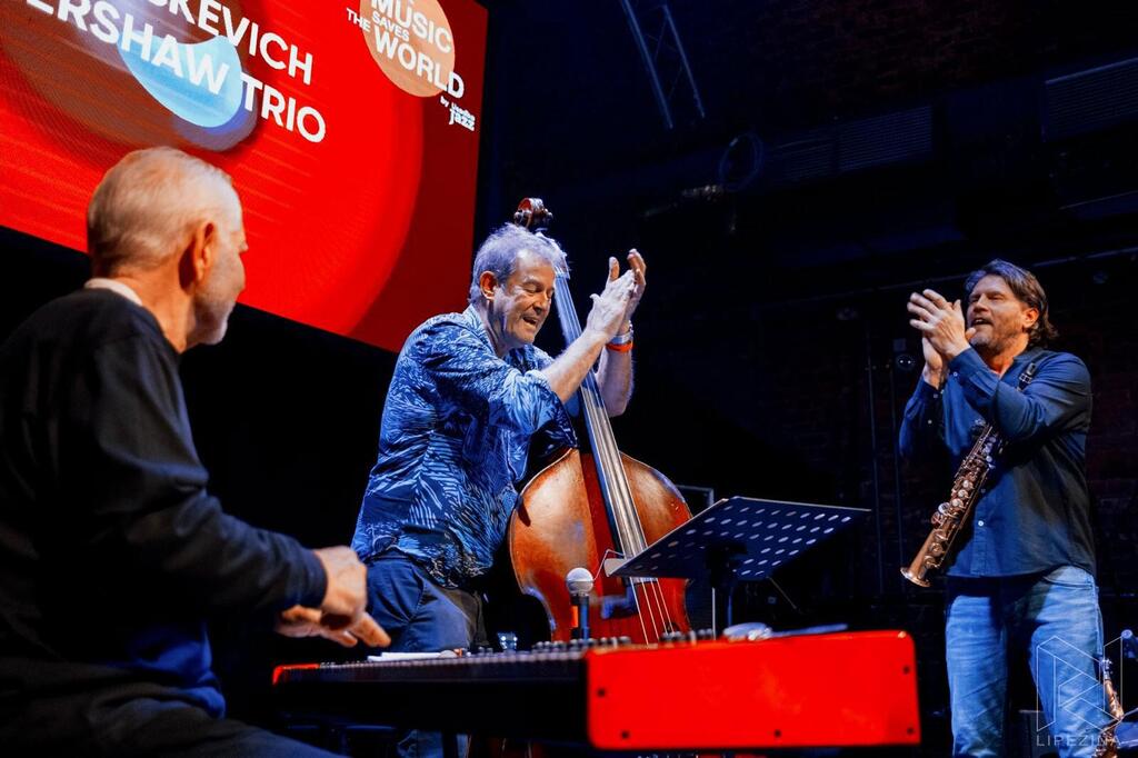 El Vintskevich-Kershaw Trio se presenta en vivo en el escenario de Londres durante el evento 'Music Saves the World' en 2024. El trío consta de un tecladista, un bajista y un saxofonista, todos comprometidos en su actuación.