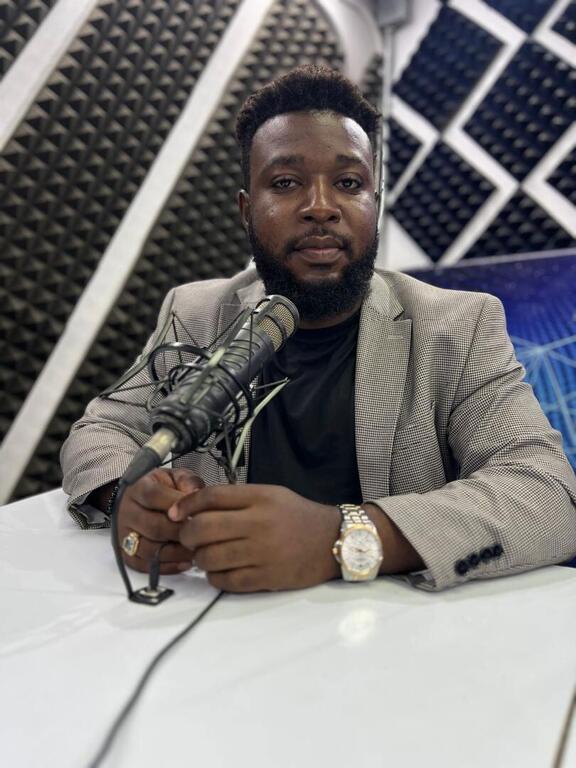 Jean Daniel S&eacute;nat, a journalist and radio host, sits at a desk with a microphone in a studio setting.