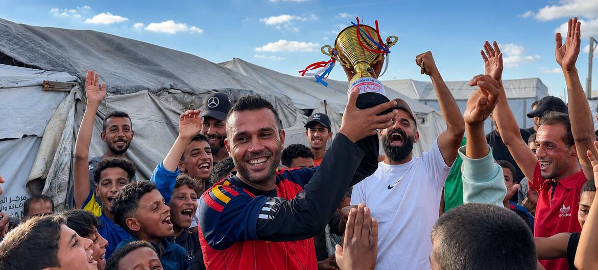 لاعب كرة القدم الفلسطيني أسعد العزابي يحمل كأس بطولة مخيمات نازحي رفح، يحتفل مع حشد من الشباب والأطفال في مواصي خان يونس.