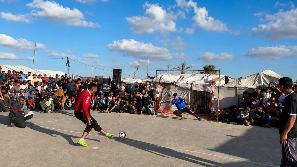 Un joueur de football palestinien frappe un ballon de football lors d'un match dans un camp de réfugiés, tandis que des spectateurs regardent depuis les tribunes.