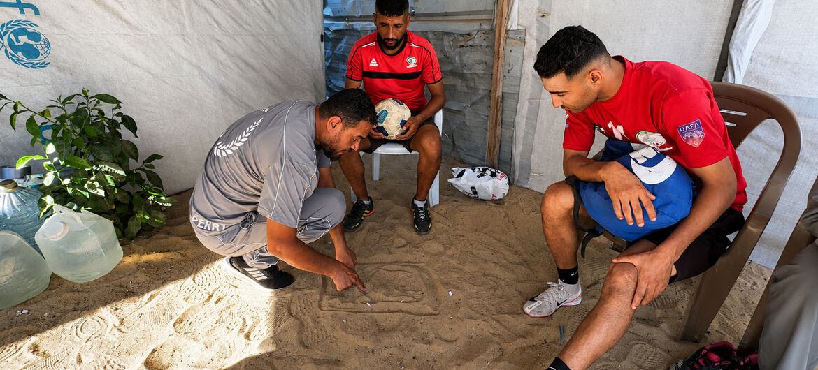 لاعب كرة القدم الفلسطيني أسعد العزابي (يمين) يستمع إلى تعليمات محمد العالول (يسار) مدرب فريق "مخيم الرحمة"، الذي يقيم به نازحون من رفح، والواقع في مواصي خان يونس.