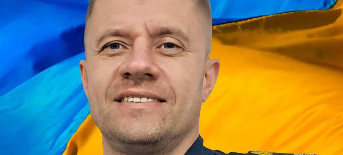 Портрет украинского пилота вертолёта Сергея Приходко в форме с украинским флагом на заднем плане.