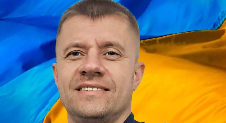Portrait of Ukrainian male helicopter pilot Sergii Prykhodko in uniform, with the Ukrainian flag in the background.