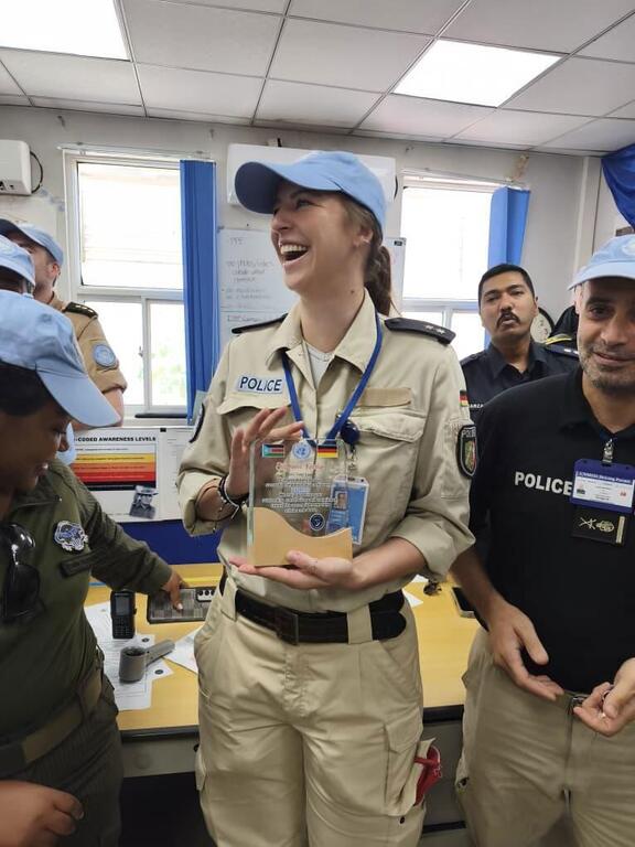 UN Woman Police Officer of the Year Stephanie K&ouml;nigs of Germany holds an award in a UNMISS office, surrounded by colleagues.