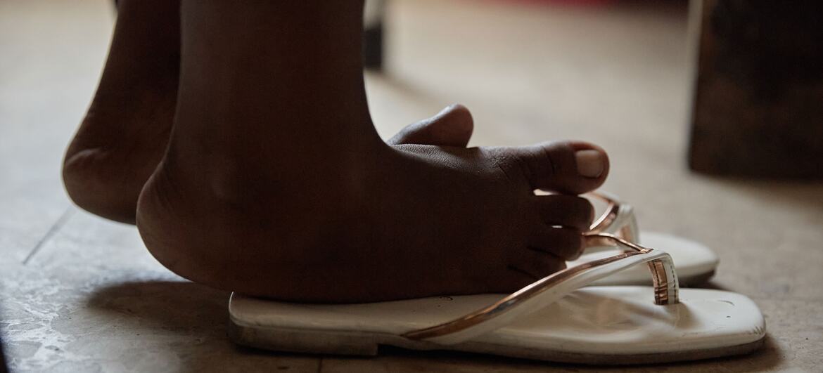 A close-up of a child's feet wearing white flip-flops on a tiled floor.