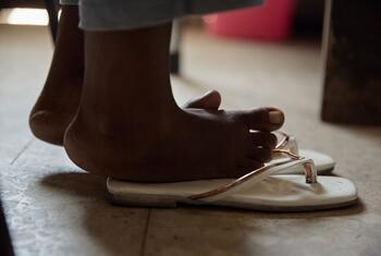 Un primer plano de los pies de un niño que lleva unas chanclas blancas sobre un suelo de baldosas.