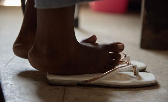 A close-up of a child's feet wearing white flip-flops on a tiled floor.