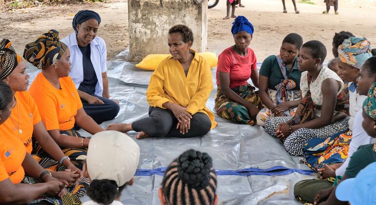 Joyce Msuya, mwakilishi wa OCHA, anakutana na kikundi cha wanawake katika mduara huko Mocimboa da Praia, Msumbiji, kama sehemu ya mpango wa mafunzo ya misaada ya kibinadamu na ustadi wa maisha. Wanawake wamekaa kwenye tarpa, wamevaa mavazi ya jadi, na wengine wamevaa vichwa. Mazingira yanaonekana kuwa nje, na muundo rahisi nyuma. Picha inachukua wakati wa ushiriki wa jamii na msaada katika eneo la baada ya mgogoro.