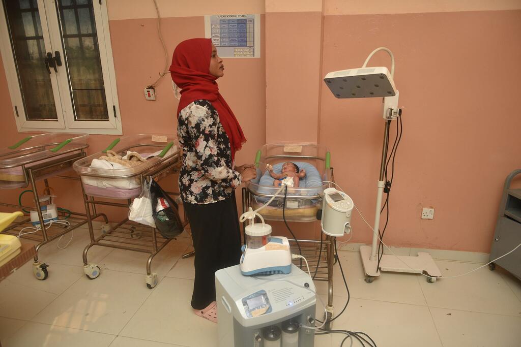A midwife in a red hijab monitors a newborn baby in an incubator at El Obeid Maternity Hospital in Sudan. The hospital opened a new neonatal unit in 2026 with only four beds, highlighting the urgent need for expanded capacity.