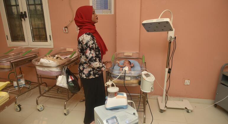 A midwife in a red hijab monitors a newborn baby in an incubator at El Obeid Maternity Hospital in Sudan. The hospital opened a new neonatal unit in 2026 with only four beds, highlighting the urgent need for expanded capacity.