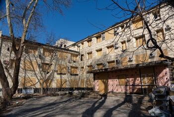 A damaged multi-story building with boarded-up windows and debris in the foreground, identified as Odesa Maternity Hospital No. 5 in Ukraine.