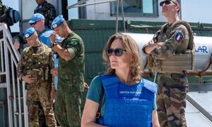Kandice Ardiel, una portavoz femenina de la UNIFIL, con un chaleco azul de las Naciones Unidas y gafas de sol, de pie frente a varios hombres de la fuerza de paz con uniformes militares.