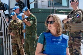 Kandice Ardiel, una portavoz femenina de la UNIFIL, con un chaleco azul de las Naciones Unidas y gafas de sol, de pie frente a varios hombres de la fuerza de paz con uniformes militares.
