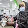 Uma refugiada sudanesa usando uma máscara e um lenço conta dinheiro em um balcão durante um programa de assistência em dinheiro do ACNUR no Egito.