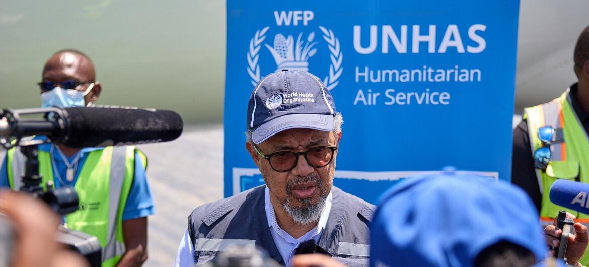 Le directeur général de l'OMS, Tedros Adhanom Ghebreyesus, s'exprime lors d'un événement de presse, avec une bannière du PAM UNHAS en arrière-plan et le personnel médiatique en train de filmer.