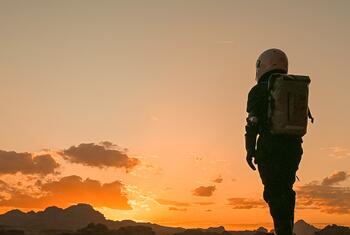 Sahbaa Shawa، زعيم الشباب في أهداف التنمية المستدامة 2025، يقف في مشهد صحاري عند غروب الشمس يرتدي بدلة رائد فضاء خلال أول مهمة مشابهة للأردن.