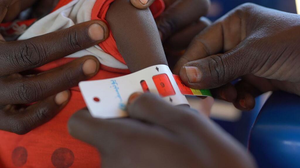 Picha ya karibu ya mikono kwa kutumia mkanda wa kupima ili kutathmini urefu wa mkono wa mtoto katika kituo cha lishe kinachoungwa mkono na UNICEF huko Tawila, Darfur Kaskazini, Sudan, kwa kugundua upungufu wa lishe mapema.