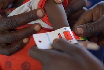 A close-up of hands using a measuring tape to assess a child's arm circumference at a UNICEF-supported nutrition center in Tawila, North Darfur, Sudan, for early detection of malnutrition.