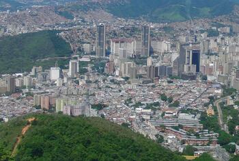 Vue aérienne de Caracas, au Venezuela, montrant un mélange de gratte-ciel modernes et de zones résidentielles densément peuplées nichées parmi des collines vertes.