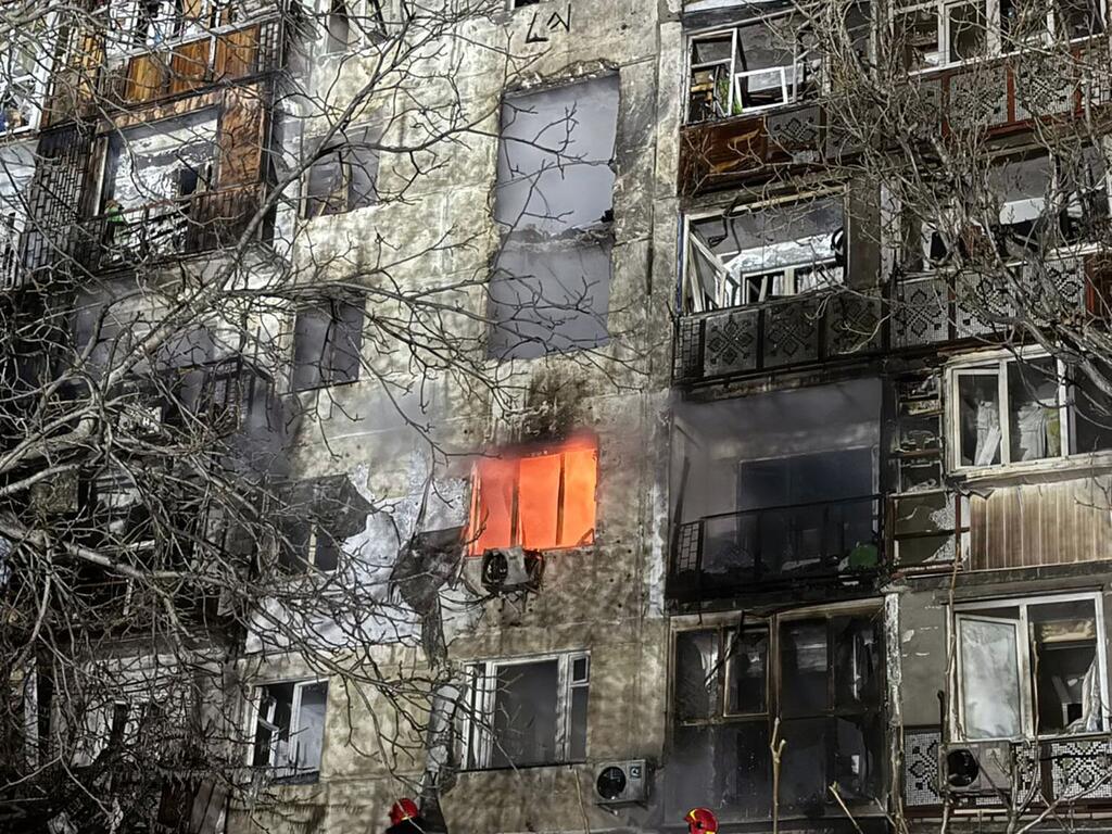 Поврежденное здание в городе Одесса, в одном из окна которого все еще горит огонь, окруженное голыми деревьями.
