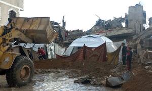 Los niños se encuentran cerca de un campamento de tiendas improvisadas en los escombros de edificios destruidos en la Franja de Gaza, ya que las fuertes lluvias e inundaciones han barrido la zona, con un vehículo amarillo de construcción parcialmente sumergido en el agua fangosa.
