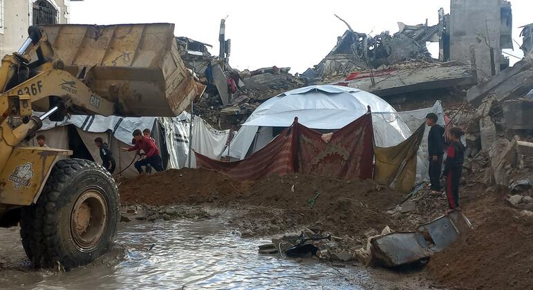 Los niños se encuentran cerca de una tienda improvisada en medio de escombros e inundaciones mientras las fuertes lluvias abarcan Gaza.