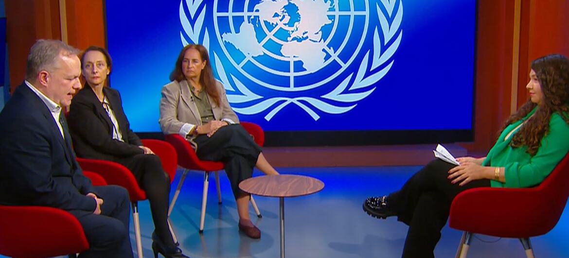 Un panel de discusión en un estudio de televisión con un gran logotipo de las Naciones Unidas en el fondo. Cuatro personas están sentadas en sillas rojas alrededor de una pequeña mesa.