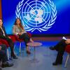 Un panel de discusión en un estudio de televisión con un gran logotipo de las Naciones Unidas en el fondo. Cuatro personas están sentadas en sillas rojas alrededor de una pequeña mesa.