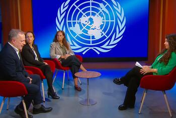 Un panel de discusión en un estudio de televisión con un gran logotipo de las Naciones Unidas en el fondo. Cuatro personas están sentadas en sillas rojas alrededor de una pequeña mesa.