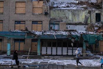 یوکرائن میں جاری جنگ کے دوران لوگ، جن میں بچے بھی شامل ہیں، ایک شدید طور پر تباہ شدہ عمارت کے پاس سے گزرتے ہیں۔