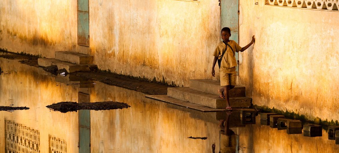 صبي يخطو على كتل حجرية لتجنب مياه الفيضانات أثناء مغادرته المدرسة في مونو، بنين.