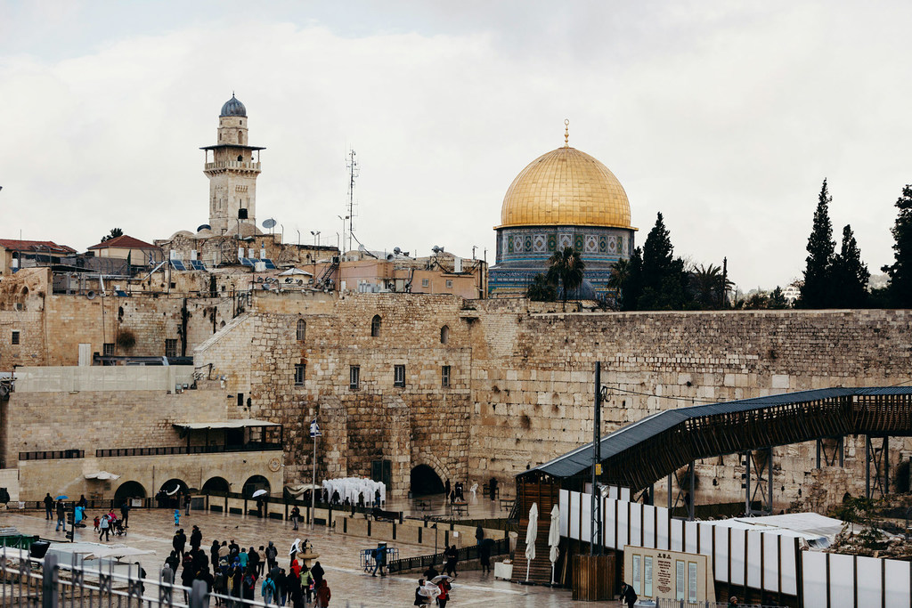 Uma vista da Cúpula da Rocha e do Muro das Lamentações em Jerusalém, Israel, com turistas na praça de pedra abaixo em um dia nublado.
