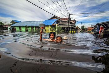 Crianças caminham pela água da enchente na Indonésia.