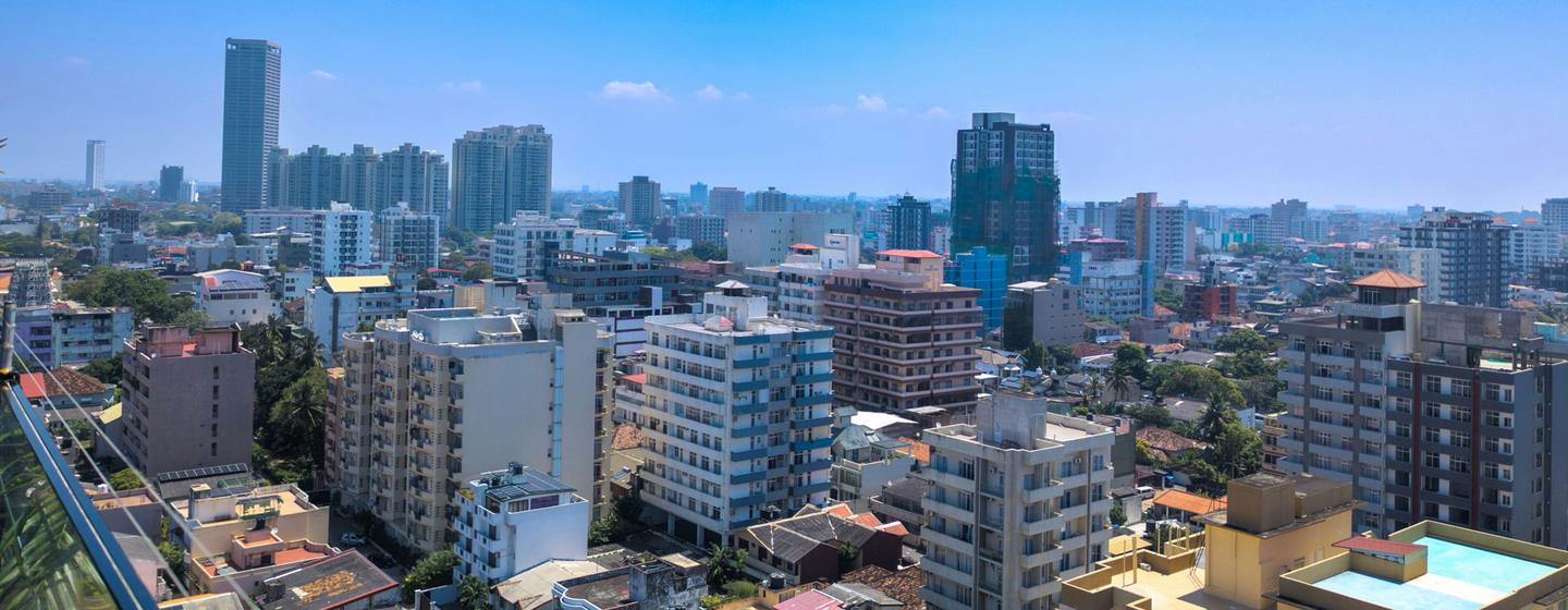 Vue panoramique de la ville de Colombo au Sri Lanka, montrant un mélange d'immeubles modernes de grande hauteur et de structures résidentielles plus basses sous un ciel bleu clair.