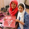 An Afghan mother and daughter hold a sign for gender equality while sitting with their handicraft products in Bamyan.