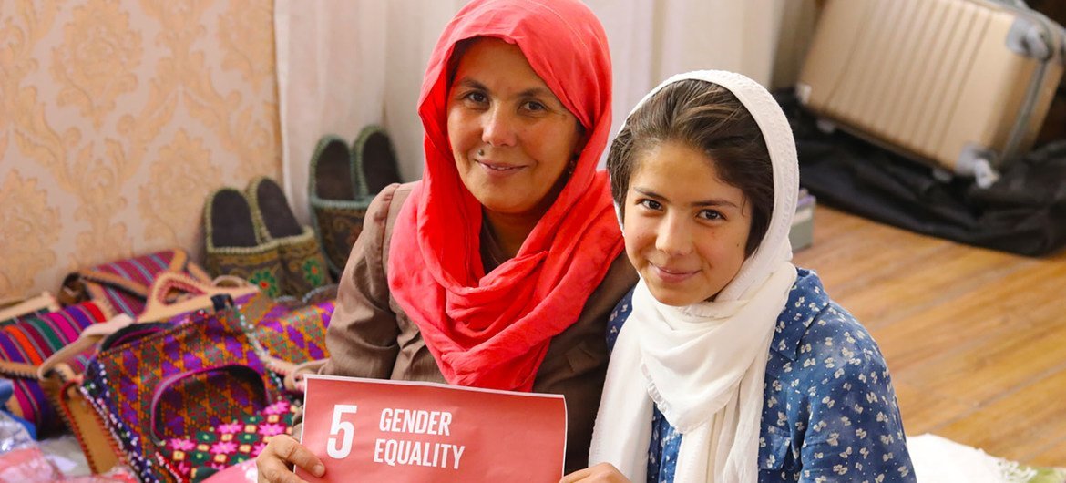 An Afghan mother and daughter hold a sign for gender equality while sitting with their handicraft products in Bamyan.