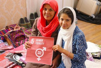 An Afghan mother and daughter hold a sign for gender equality while sitting with their handicraft products in Bamyan.