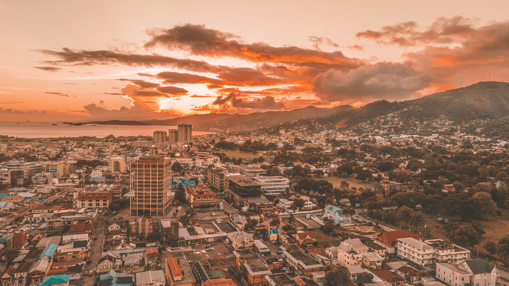 Vue aérienne de Port of Spain, à Trinité-et-Tobago, au coucher du soleil, avec la silhouette de la ville, les eaux côtières et les montagnes en arrière-plan.