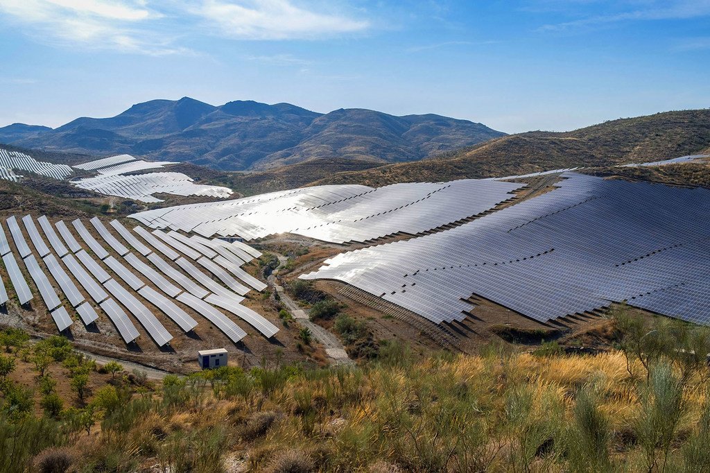 Una central de energía fotovoltaica que cubre valles y laderas en Andalucía, España, con paneles solares dispuestos en filas bajo un cielo despejado.