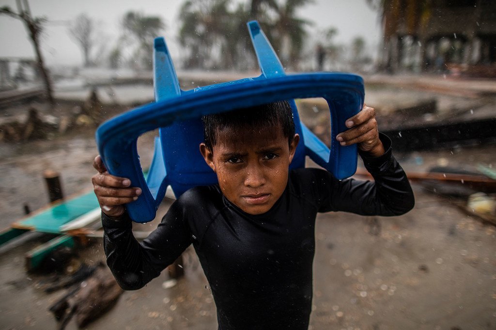 Un niño se protege de la lluvia con una silla de plástico azul en una zona inundada y llena de escombros en Bilwi, Nicaragua, tras la destrucción causada por el huracán Iota.