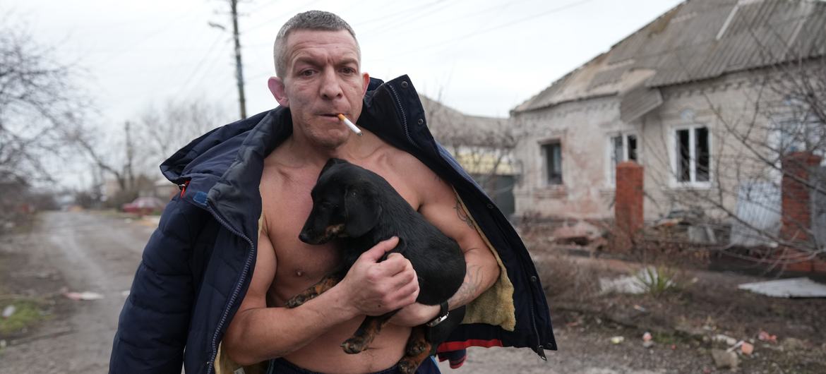 A man holds a dog as he walks past a damaged house following shelling in Mariupol, in southeastern Ukraine.